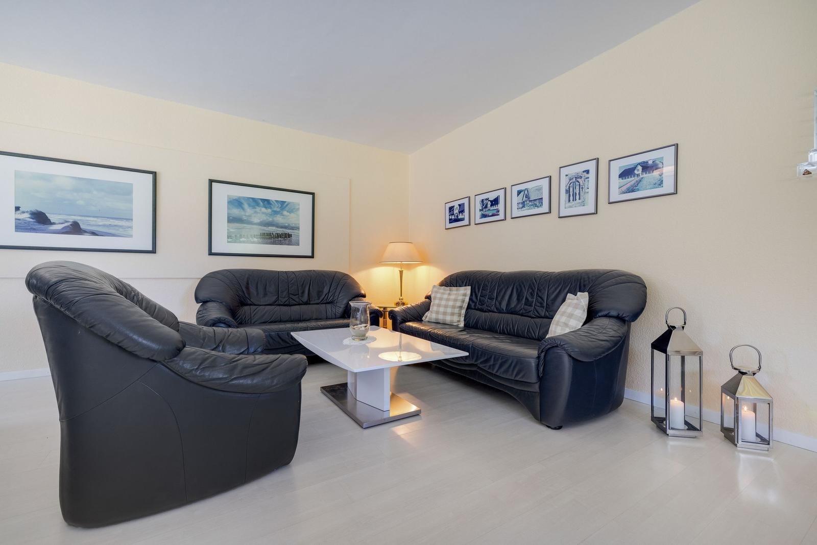 Wohnzimmer mit schwarzen Ledermöbeln, weißen Wänden und Bildern an der Wand.