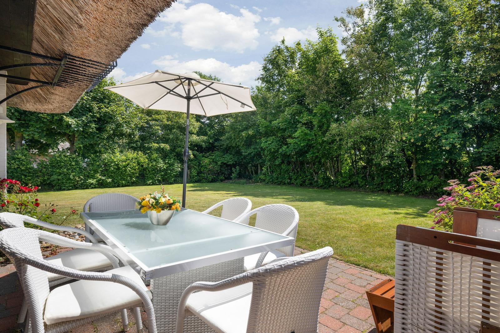 Terrasse mit weißem Tisch und Stühlen, Sonnenschutz und grünem Garten