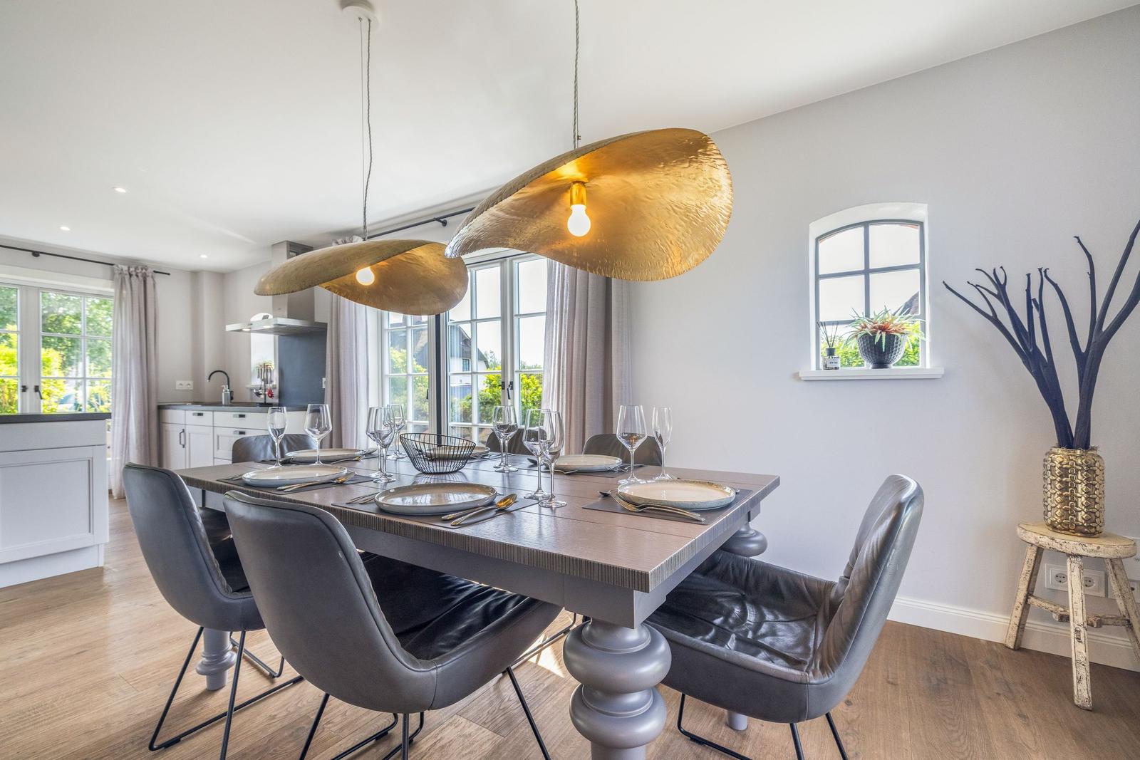 Esstisch mit Stühlen, goldene Deckenleuchten und Fenster zur Außenseite.