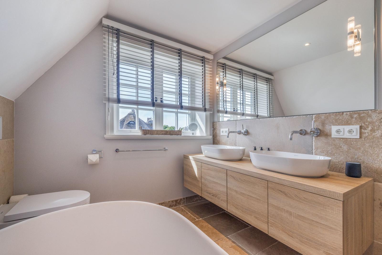 Badezimmer mit Doppelwaschbecken, Badewanne und Fenster mit Jalousie.