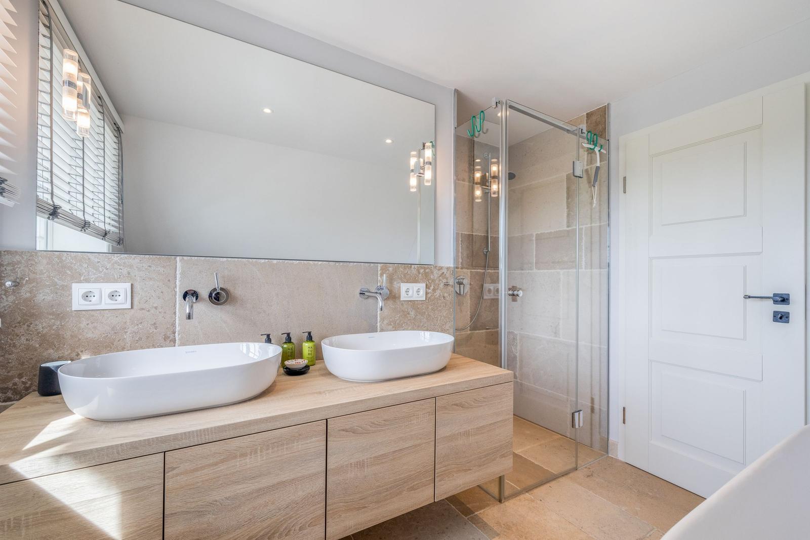 Badezimmer mit zwei Waschbecken, Spiegelschrank und Dusche mit Glaswand.