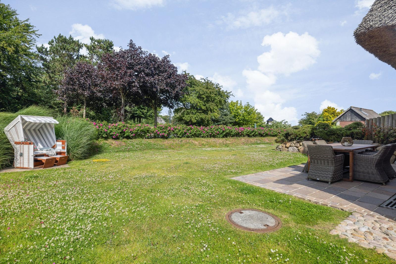 Großer Garten mit Liege, Tisch und Stühlen. Grasfläche und Blumenbeete.