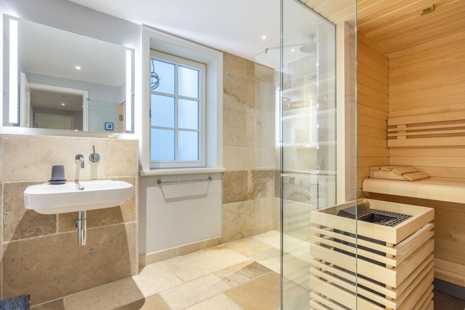 Badezimmer mit Dusche, Sauna und Waschbecken an Steinwand.