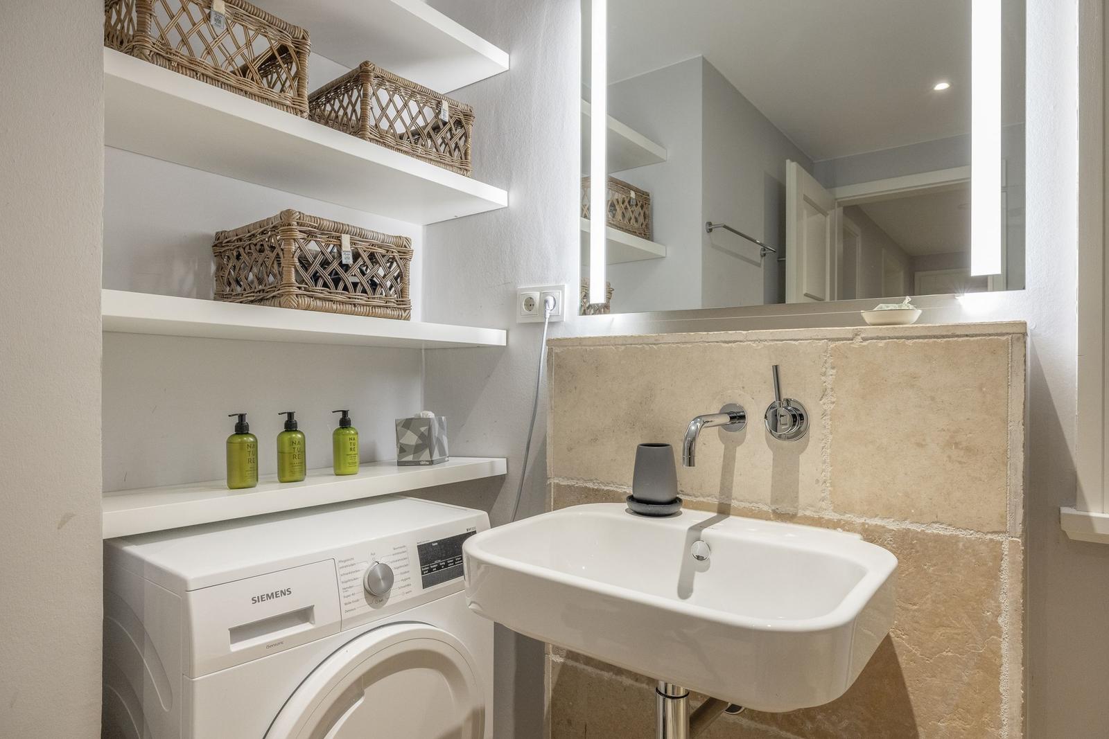 Badezimmer mit Waschmaschine, Spülbecken und beleuchtetem Spiegel.