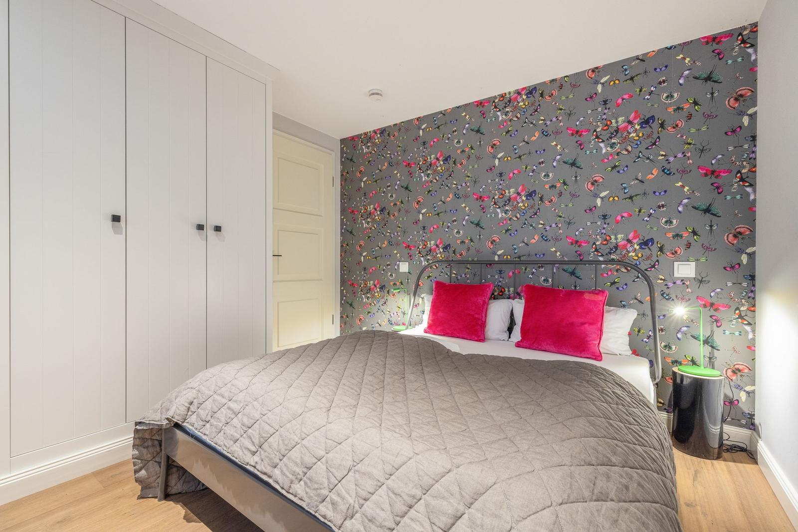 Schlafzimmer mit Bett, Schrank und Schmetterlingswandtapete.