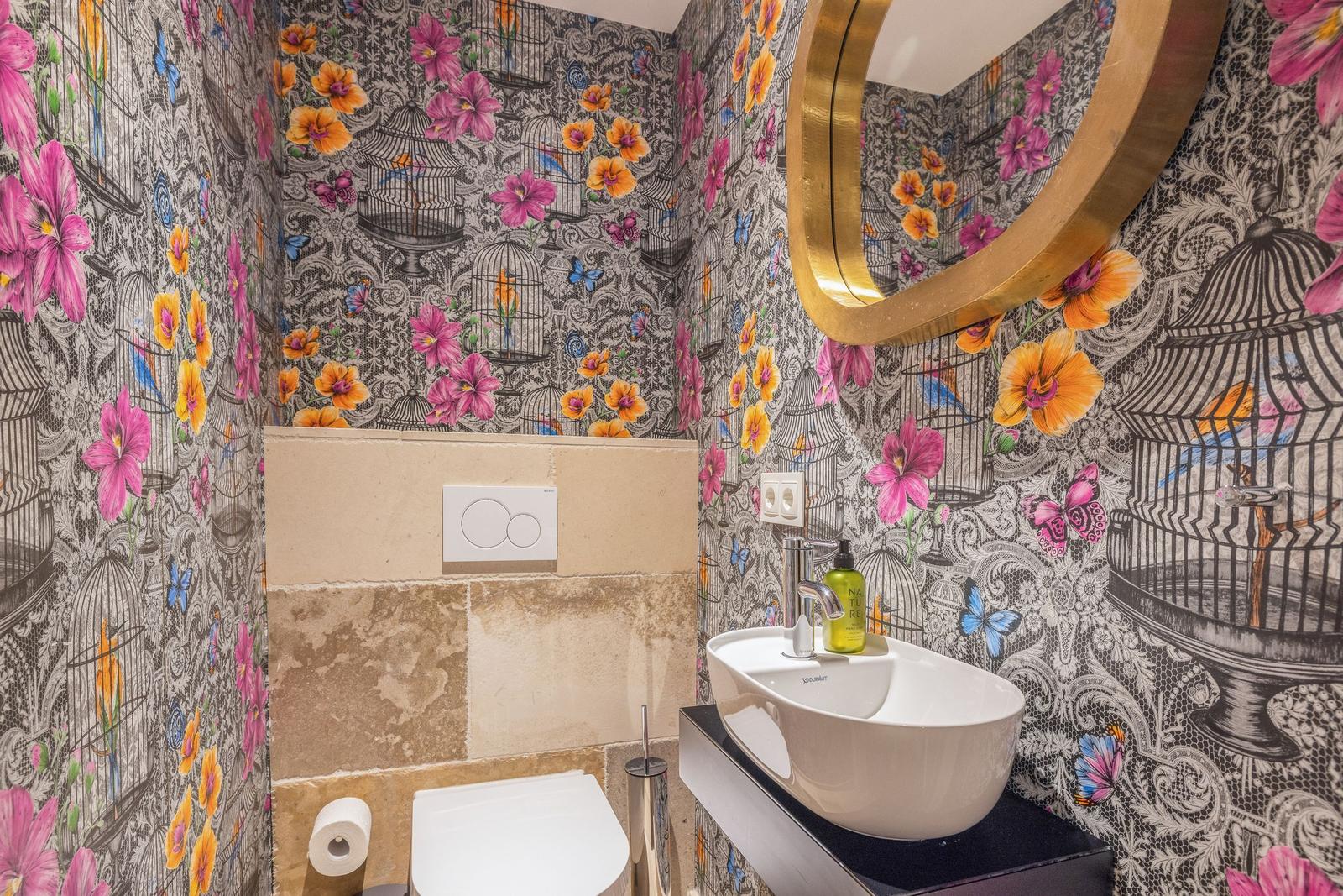 Badezimmer mit floral gemusterter Tapete, Waschbecken und Spiegel.