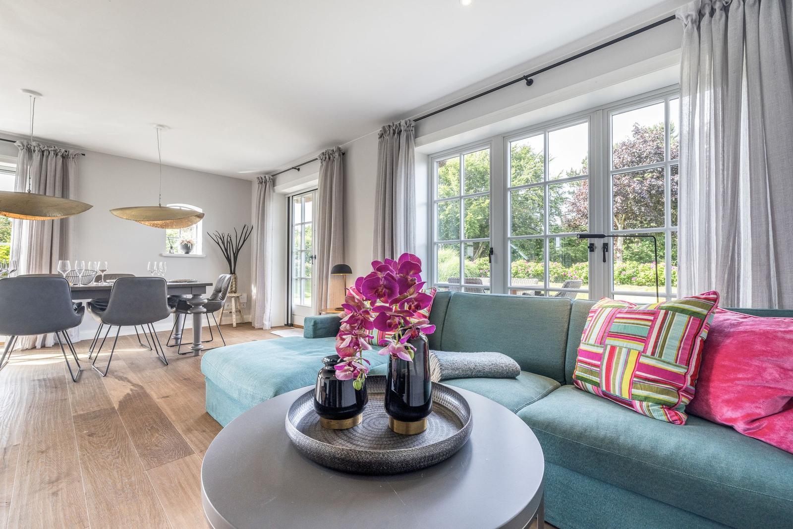 Ein Wohn- und Essbereich mit Sofa, Tisch und Fenstern zum Garten.