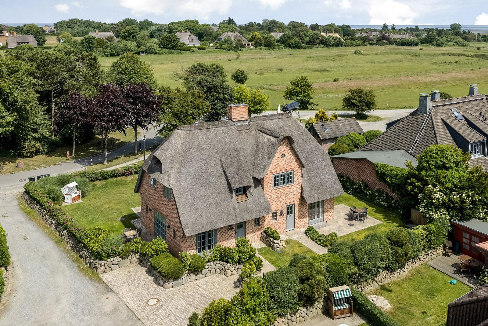 Traditionelles Haus mit Strohdach und gepflegtem Garten. Blick auf Felder und Wald.