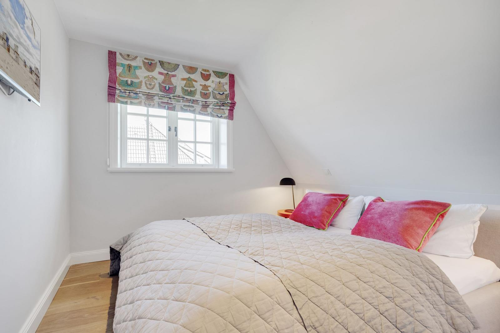 Schlafzimmer mit Dachschräge, Fenster und Bett mit Kissen.