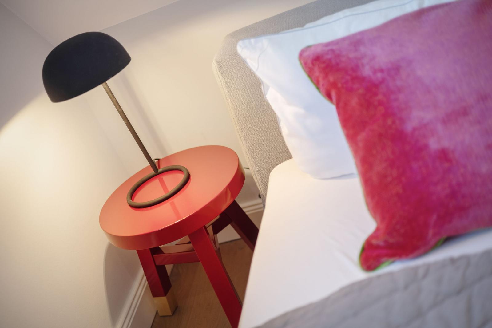 Ein Bett mit Kissen und eine rote Tischlampe auf einem roten Tisch.
