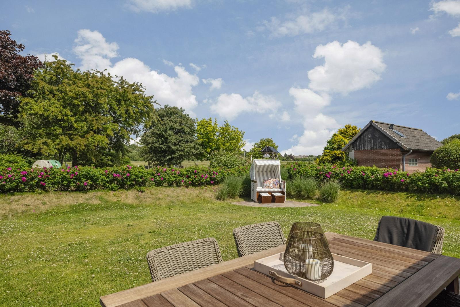 Terrasse mit Tisch und Stühlen, Blick auf Garten mit Strandkorb und Haus.
