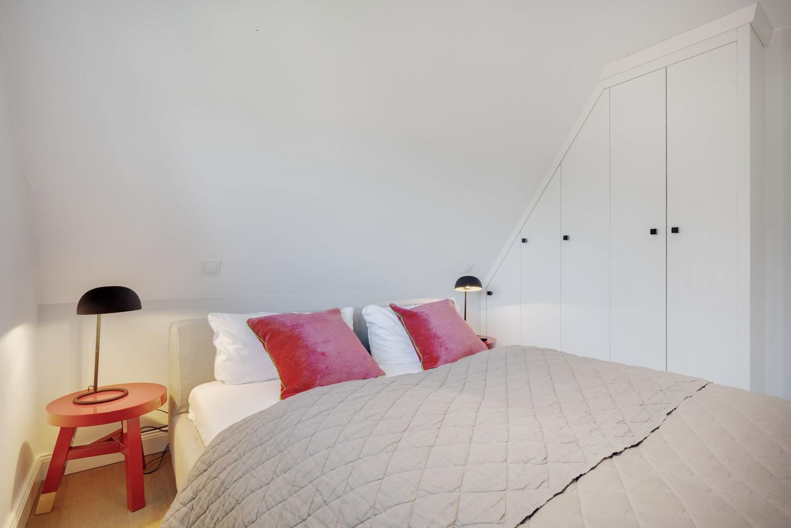 Schlafzimmer mit Bett, zwei Nachttischen und weißen Schränken an der schrägen Wand.