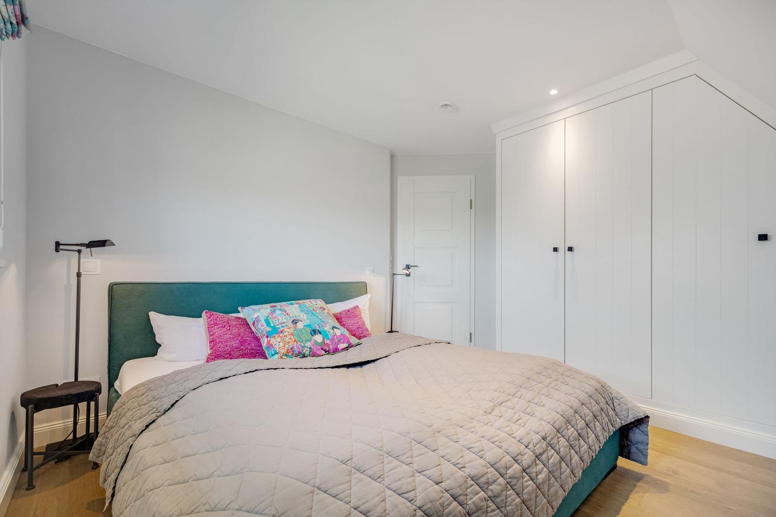 Schlafzimmer mit Bett, Kleiderschrank und Stehlampe.