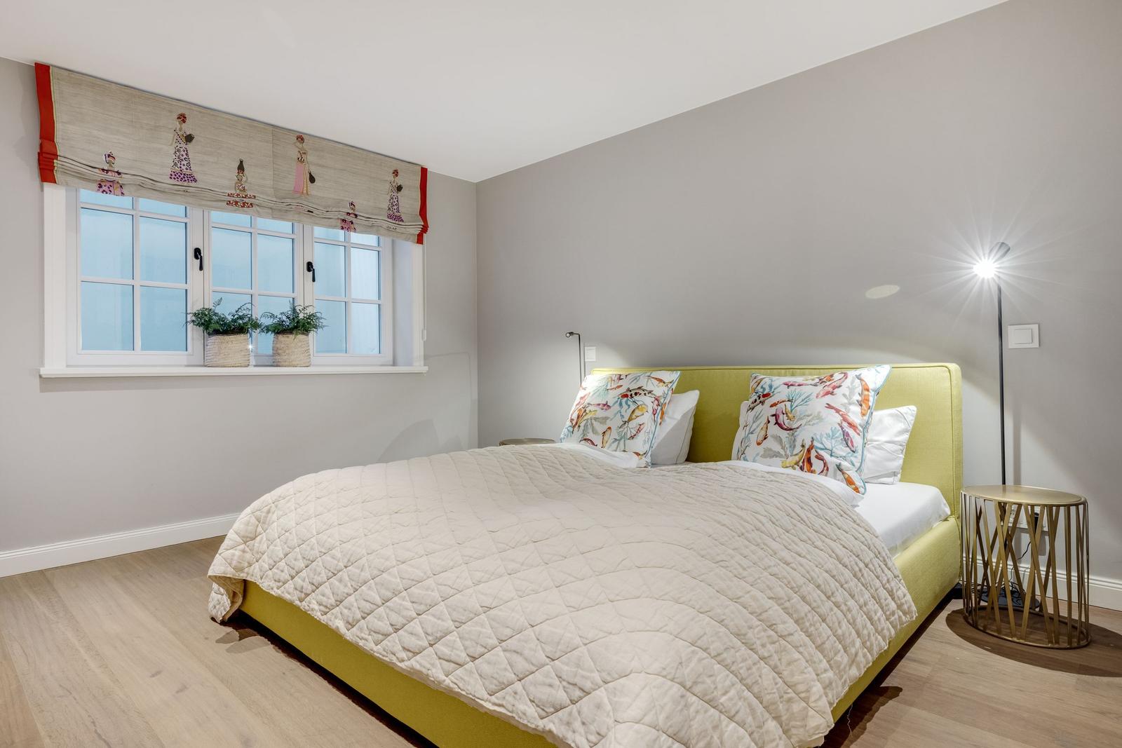 Schlafzimmer mit gelbem Bett, Fenster mit Vorhang und Stehlampe.