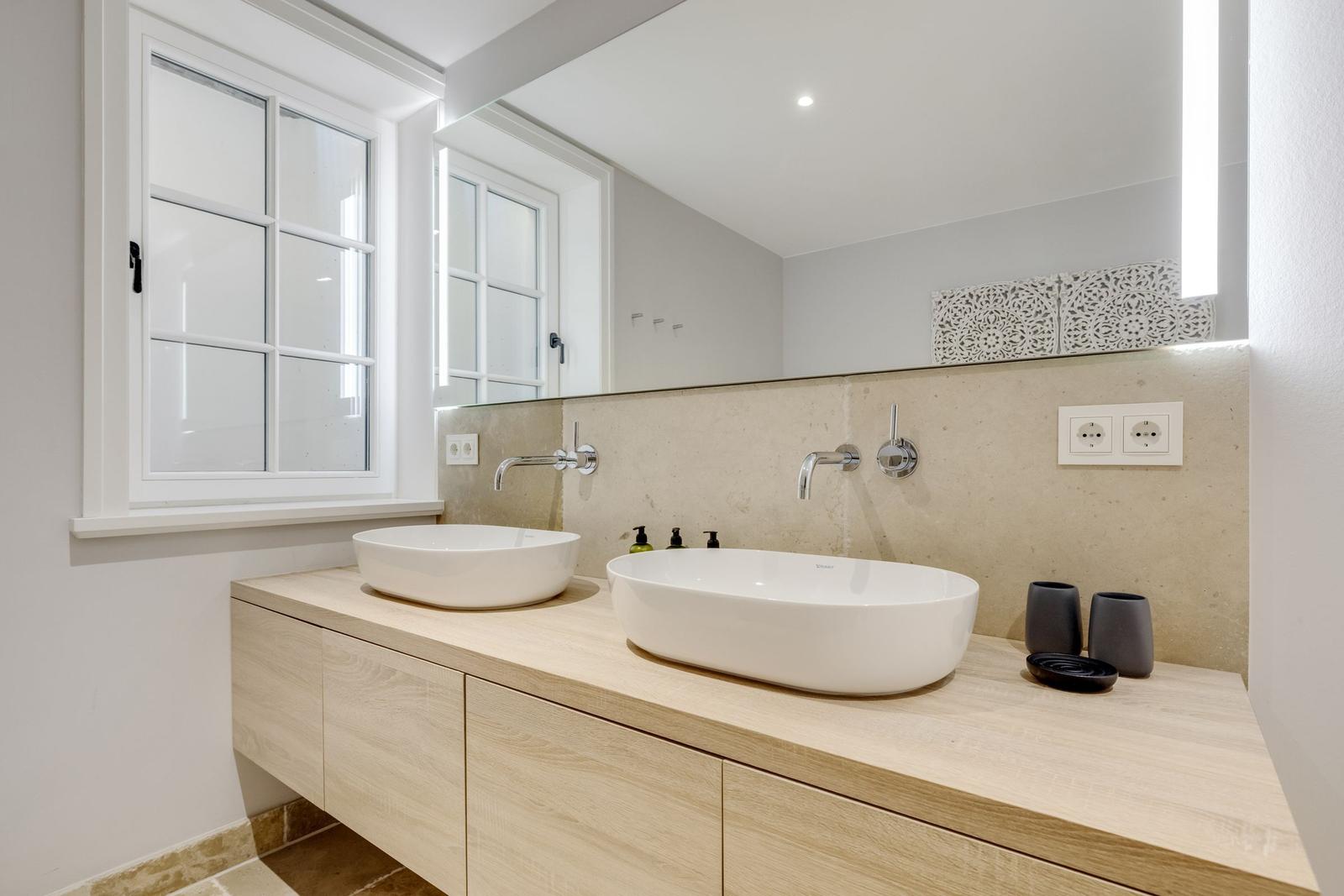 Badezimmer mit zwei Waschbecken, Holzschrank und Fenster.