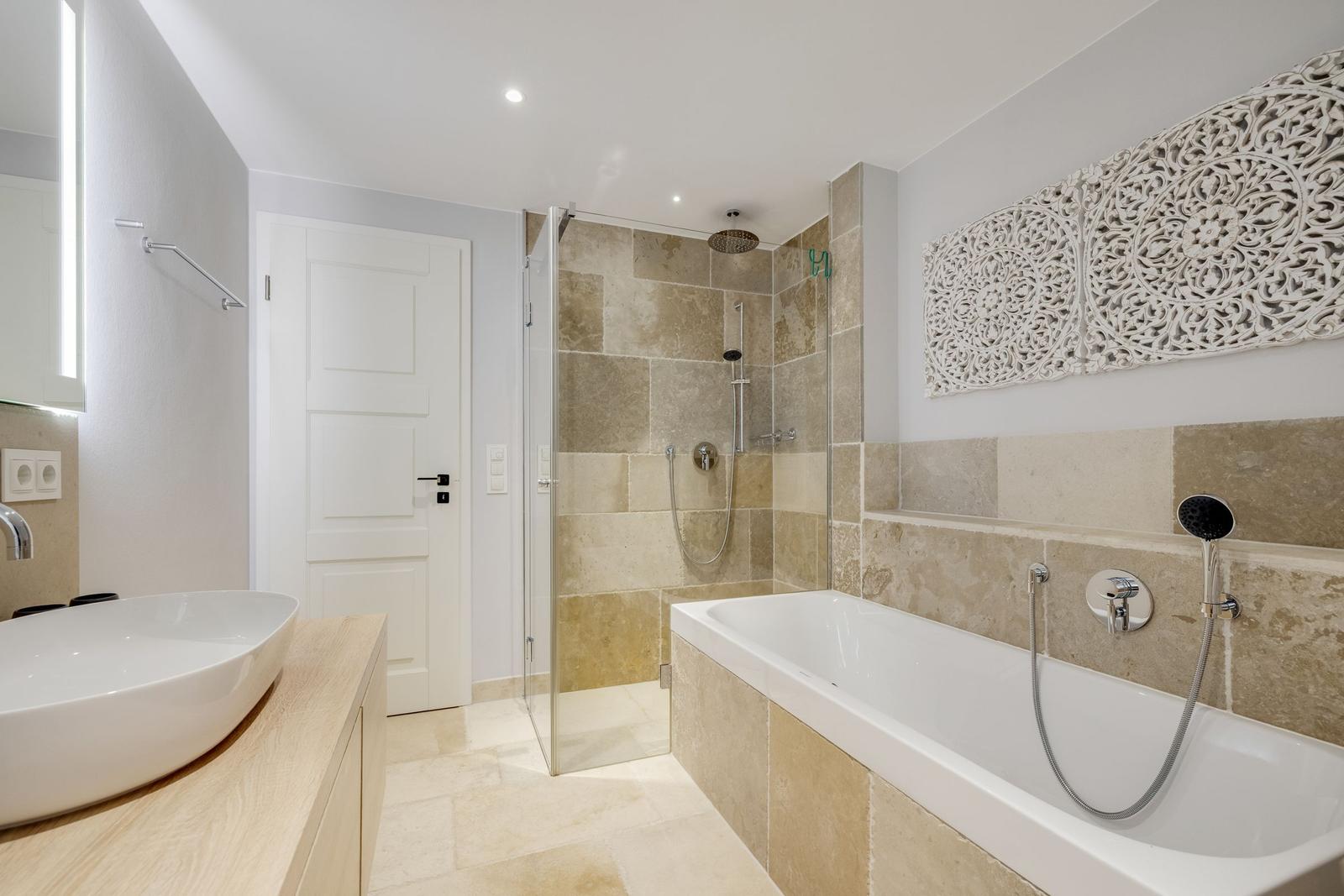 Badezimmer mit Dusche, Badewanne und Waschbecken auf Holzunterlage.
