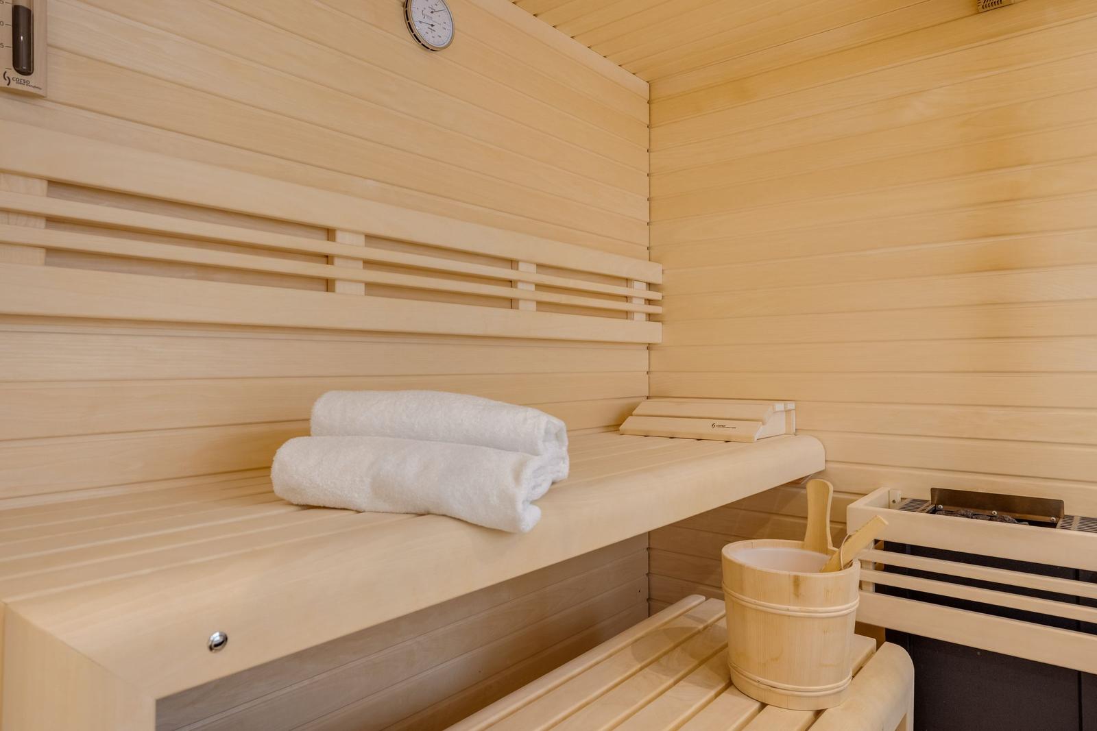 Sauna mit Holzbank, weißen Handtüchern und Eimer mit Löffel.