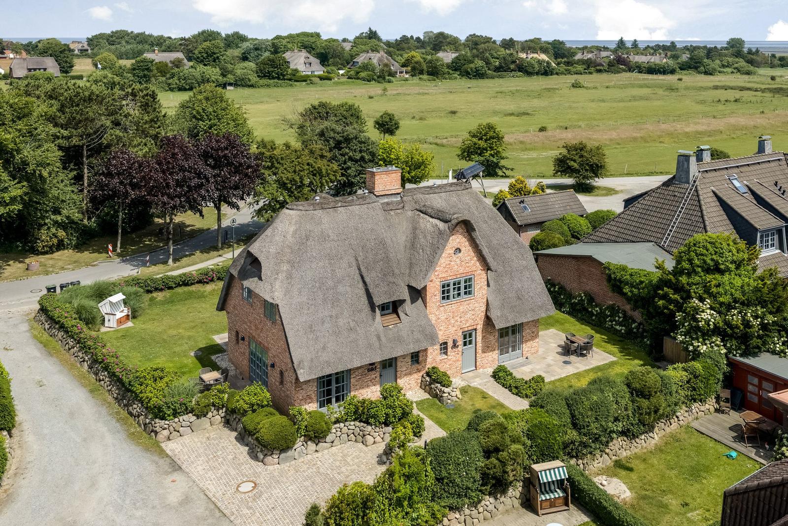Dorfhaus mit Strohdach, Garten und Terrasse. Blick auf grüne Wiesen und Wald.