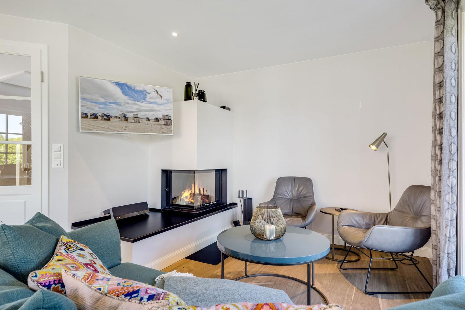 Wohnzimmer mit Kamin, Sofa, zwei Sessel und runden Tisch.