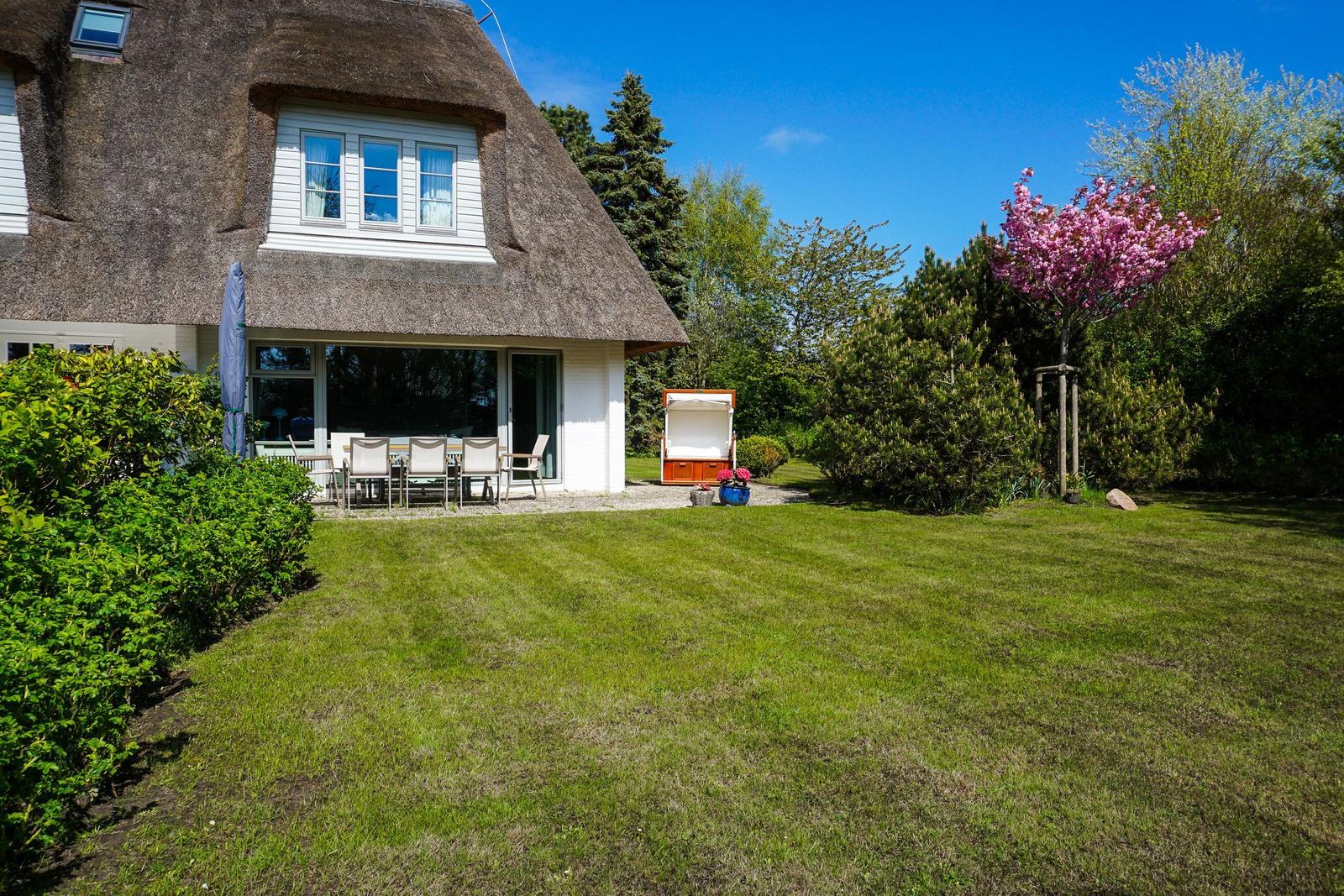 Haus mit Strohdach, Garten mit Liegestühlen und blühendem Baum.