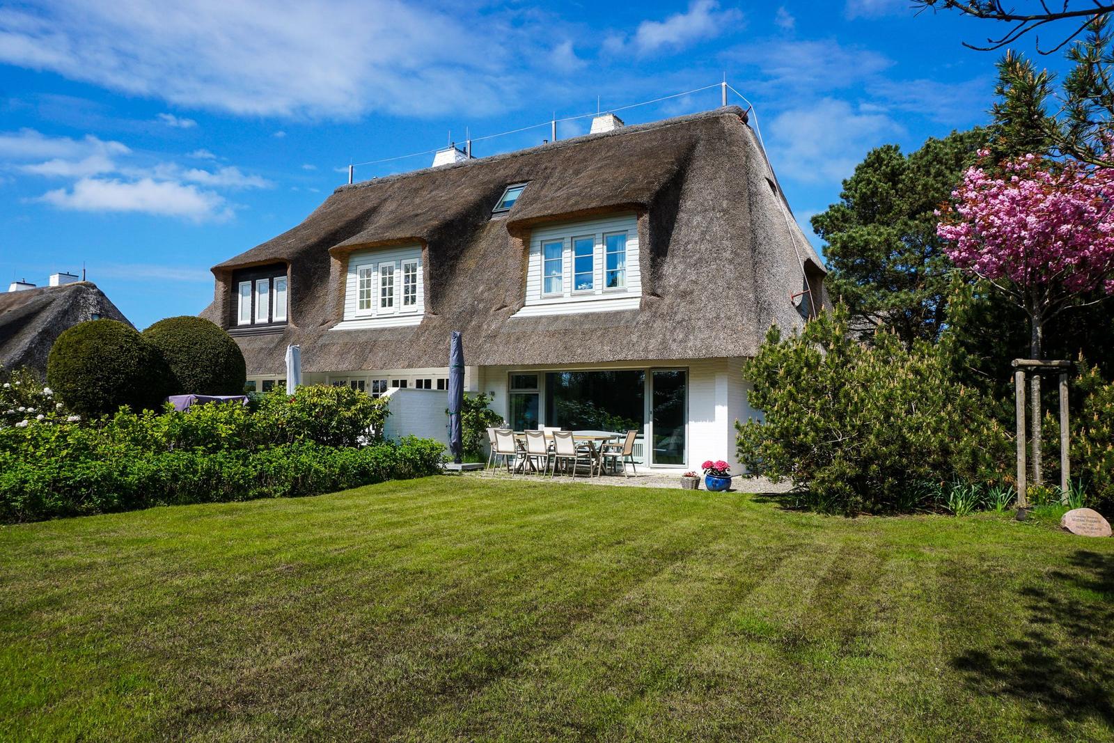 Haus mit Strohdach, Garten und Terrasse mit Tisch und Stühlen.