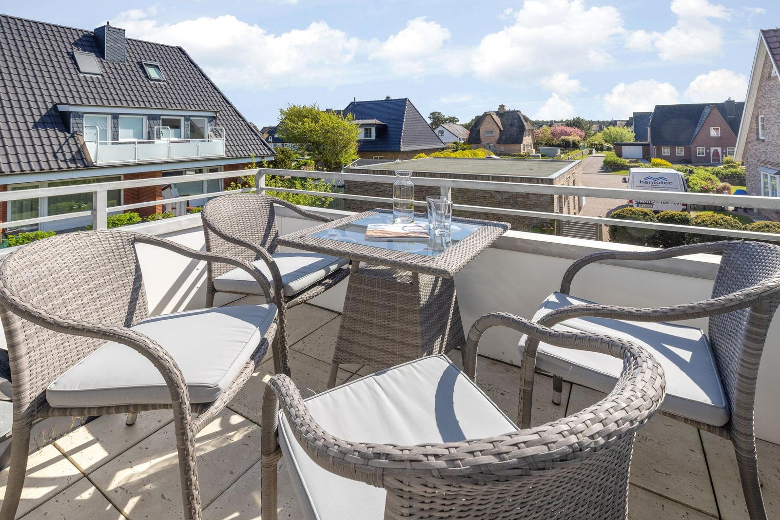 Terrace with four chairs and table. View of houses and green areas.