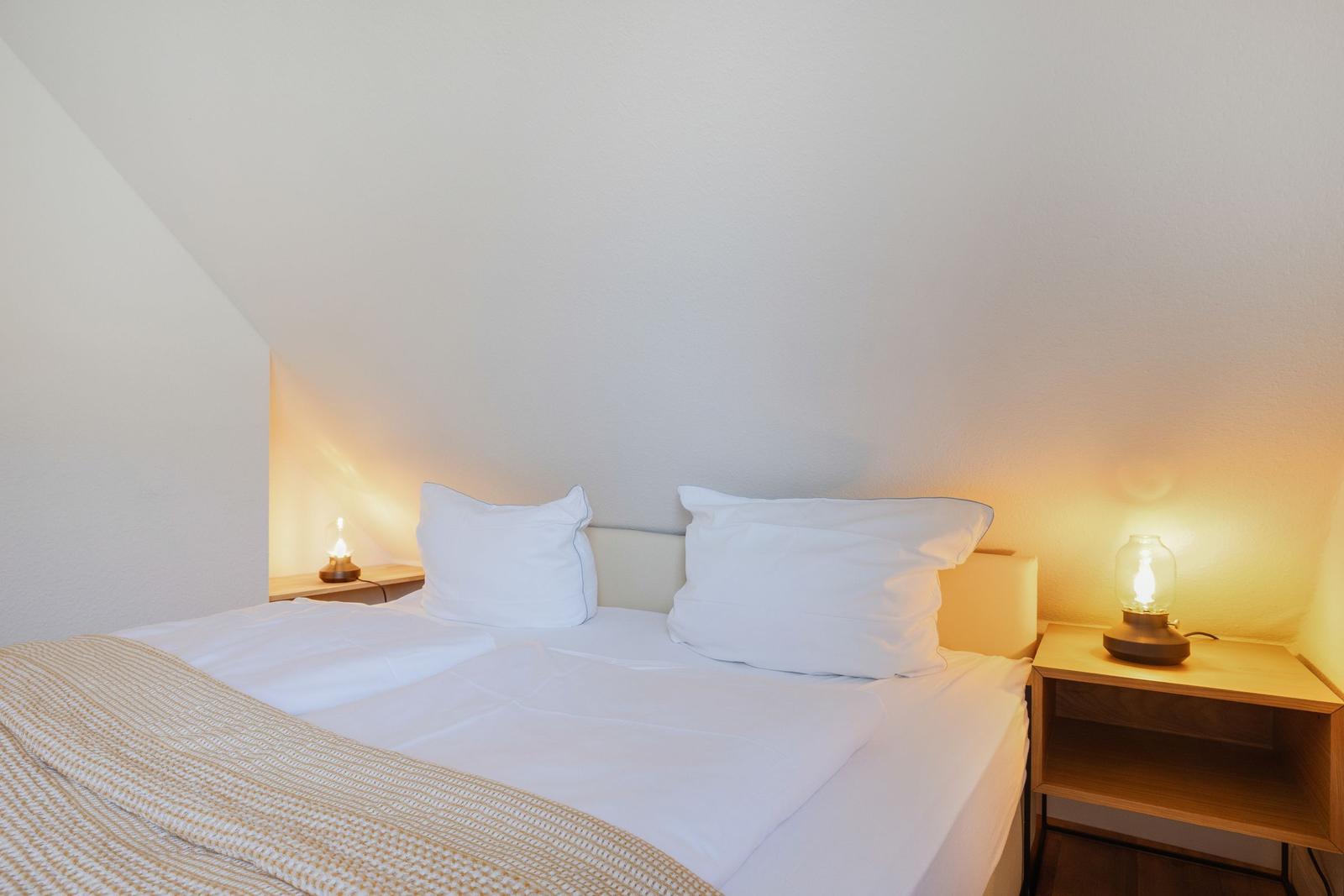 Bedroom with double bed, two nightstands, and lamps under sloped ceiling.