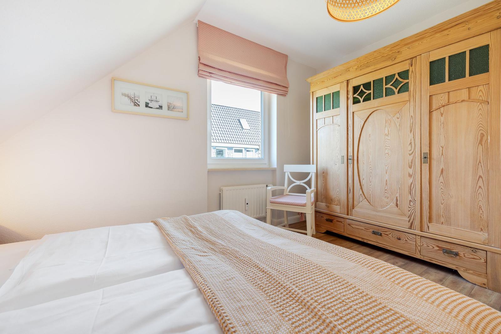 Bedroom with bed, wooden wardrobe, and window with roller blind.