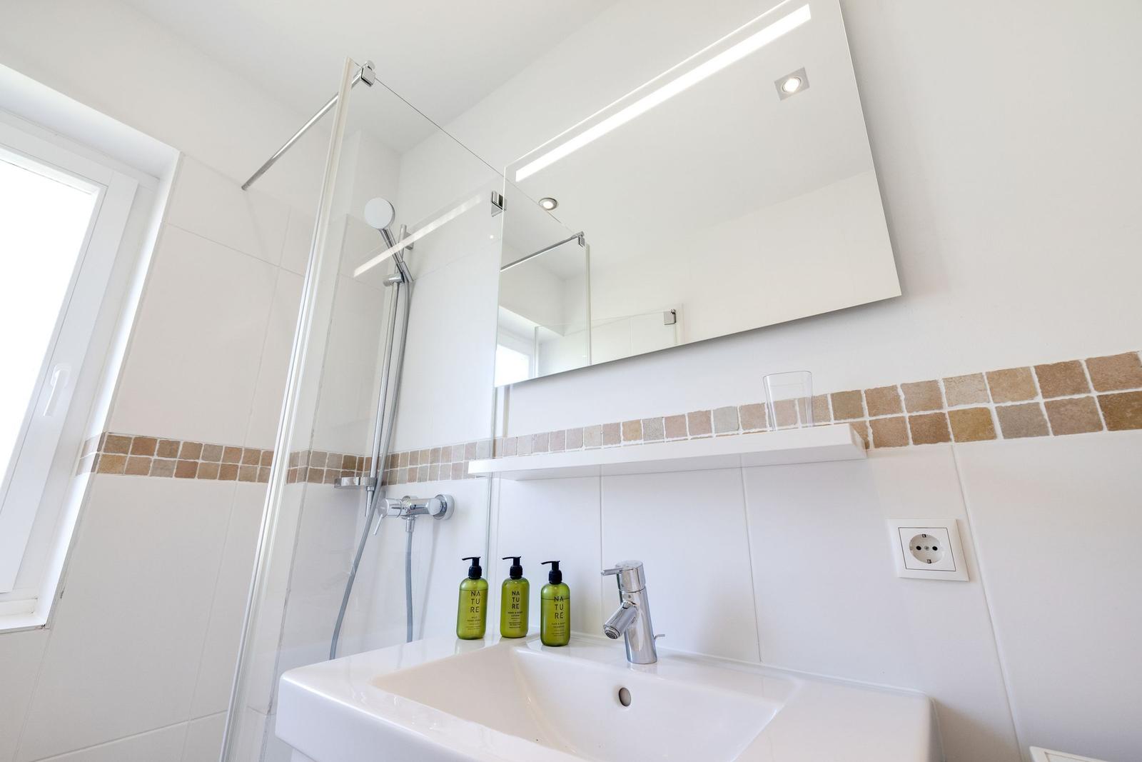 Bathroom with shower, mirror, and sink with green bottles.