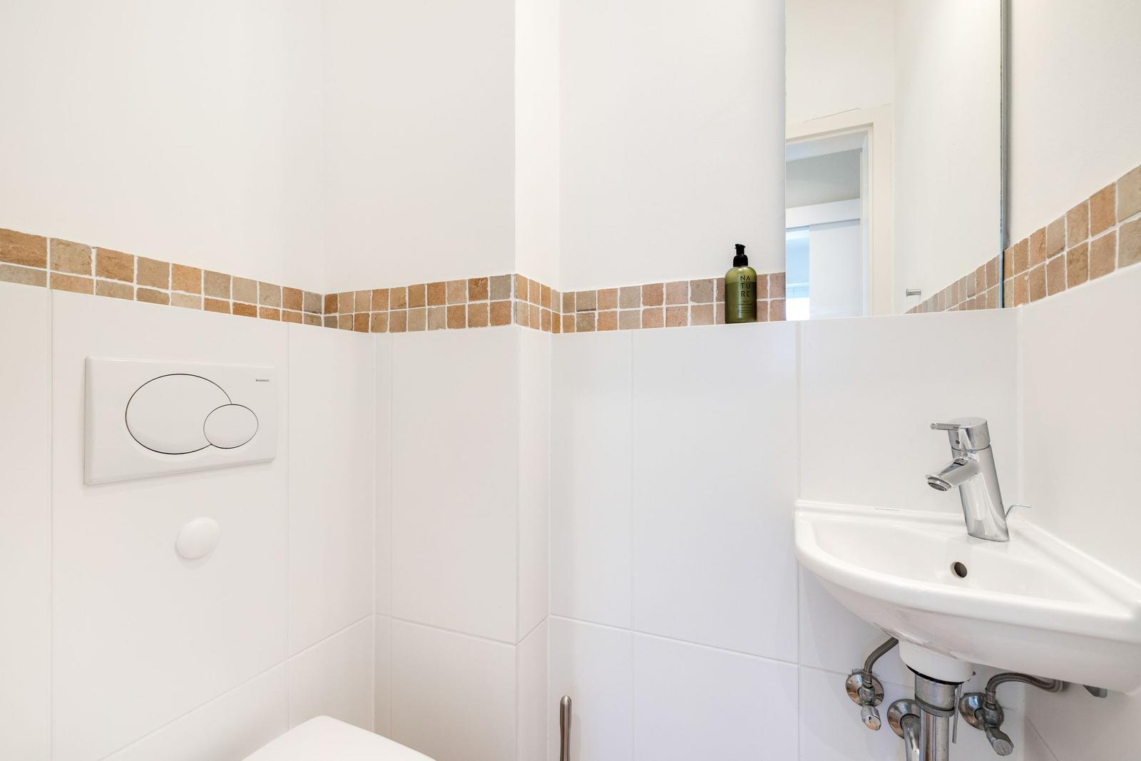 Bathroom with toilet, sink, and mirror. Wall cladding with brown tiles.