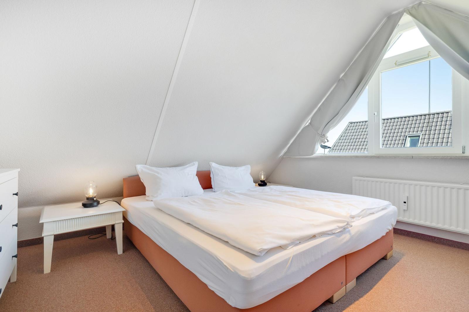 Bedroom with sloped ceiling, bed, nightstand, and window overlooking rooftops.