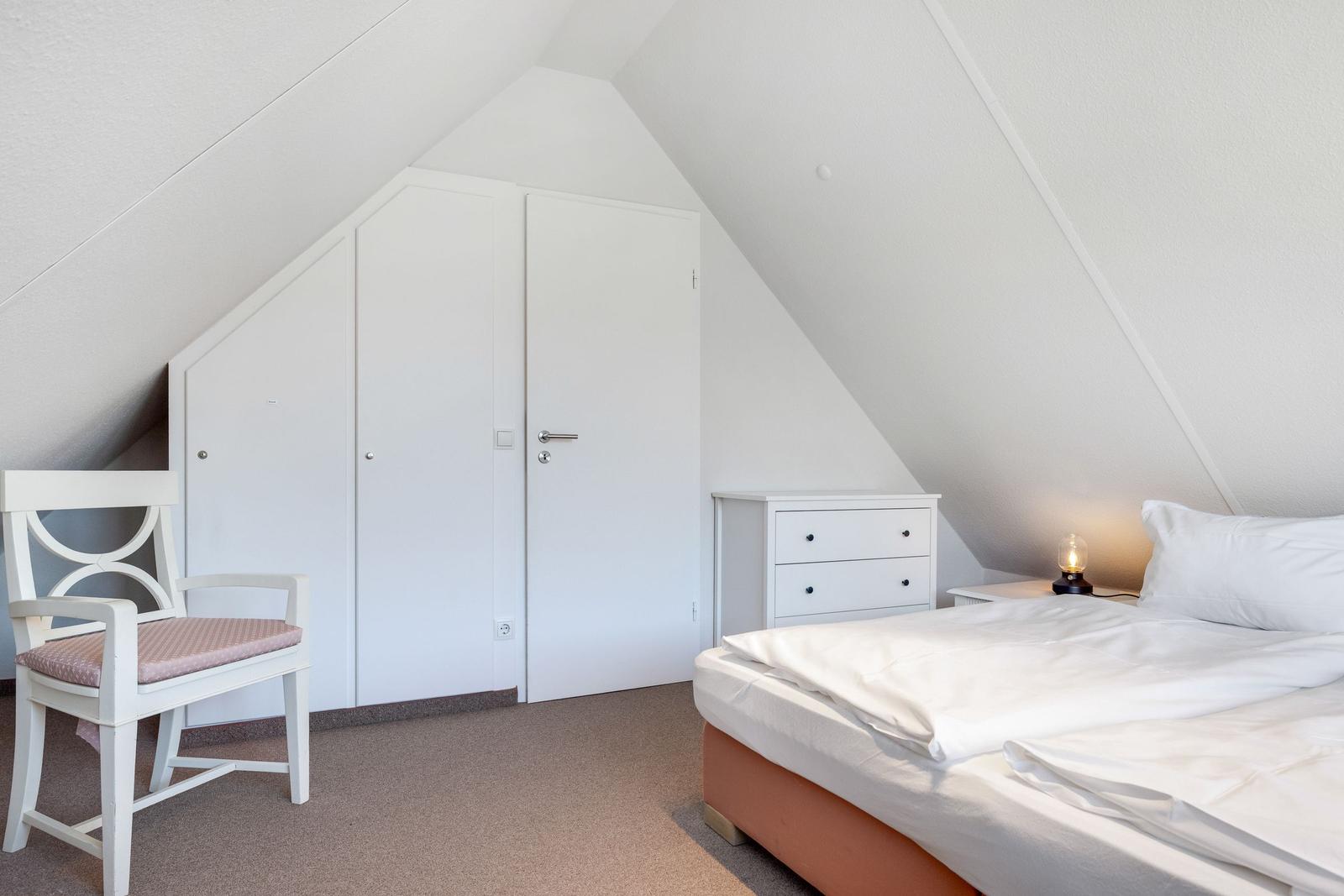 Bedroom with sloped ceiling, bed, wardrobe, and chair.