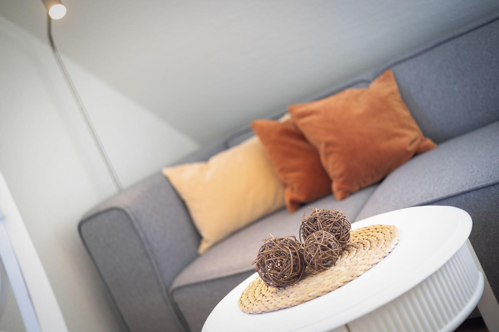 A gray sofa with orange and cream cushions. Three brown balls are on a white table.