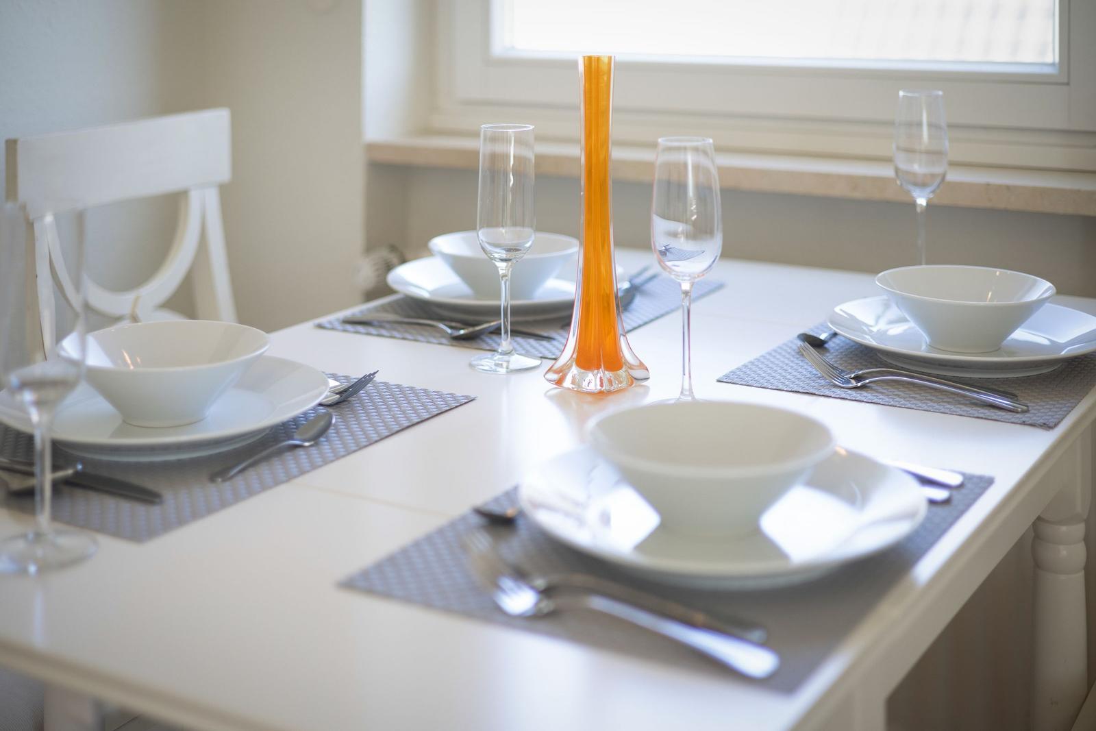 Table with white plates, glasses, and an orange vase object.