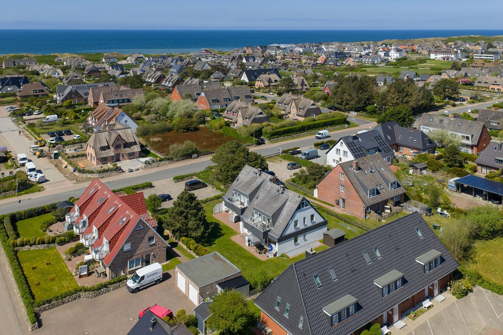 Aerial view of a coastal village with houses, roads, and the sea in the background.