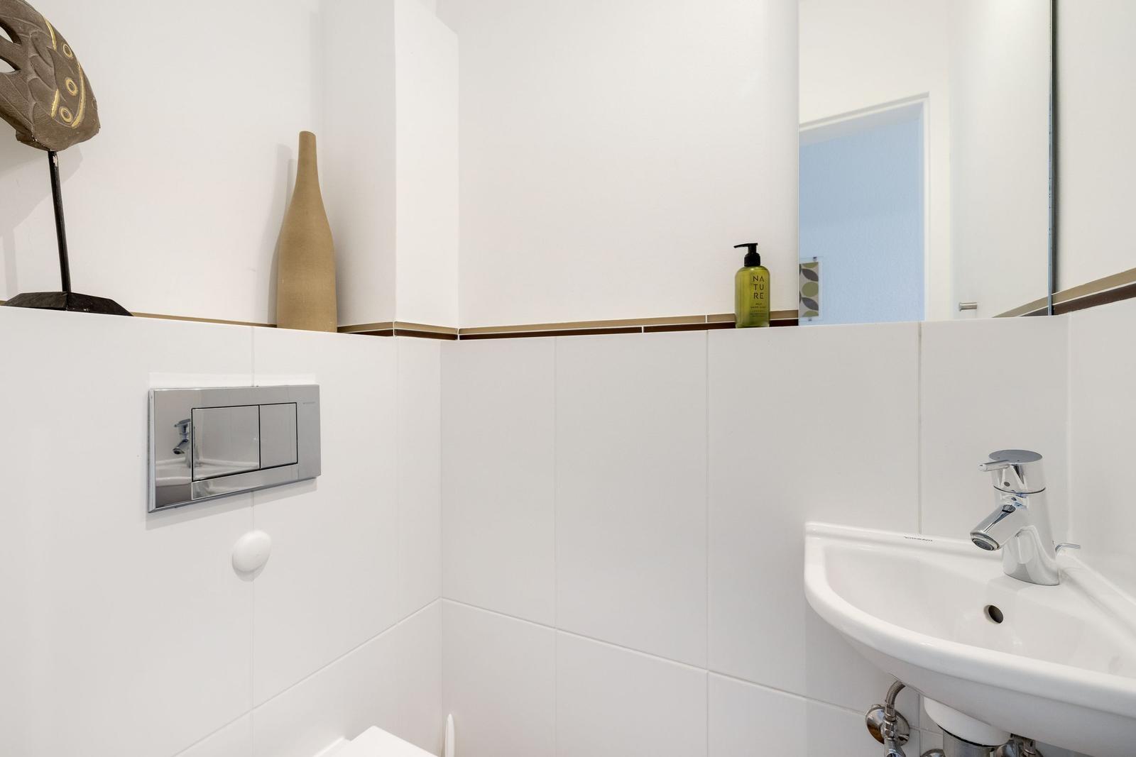 Bathroom with sink, mirror, and toilet. Walls covered with white tiles.