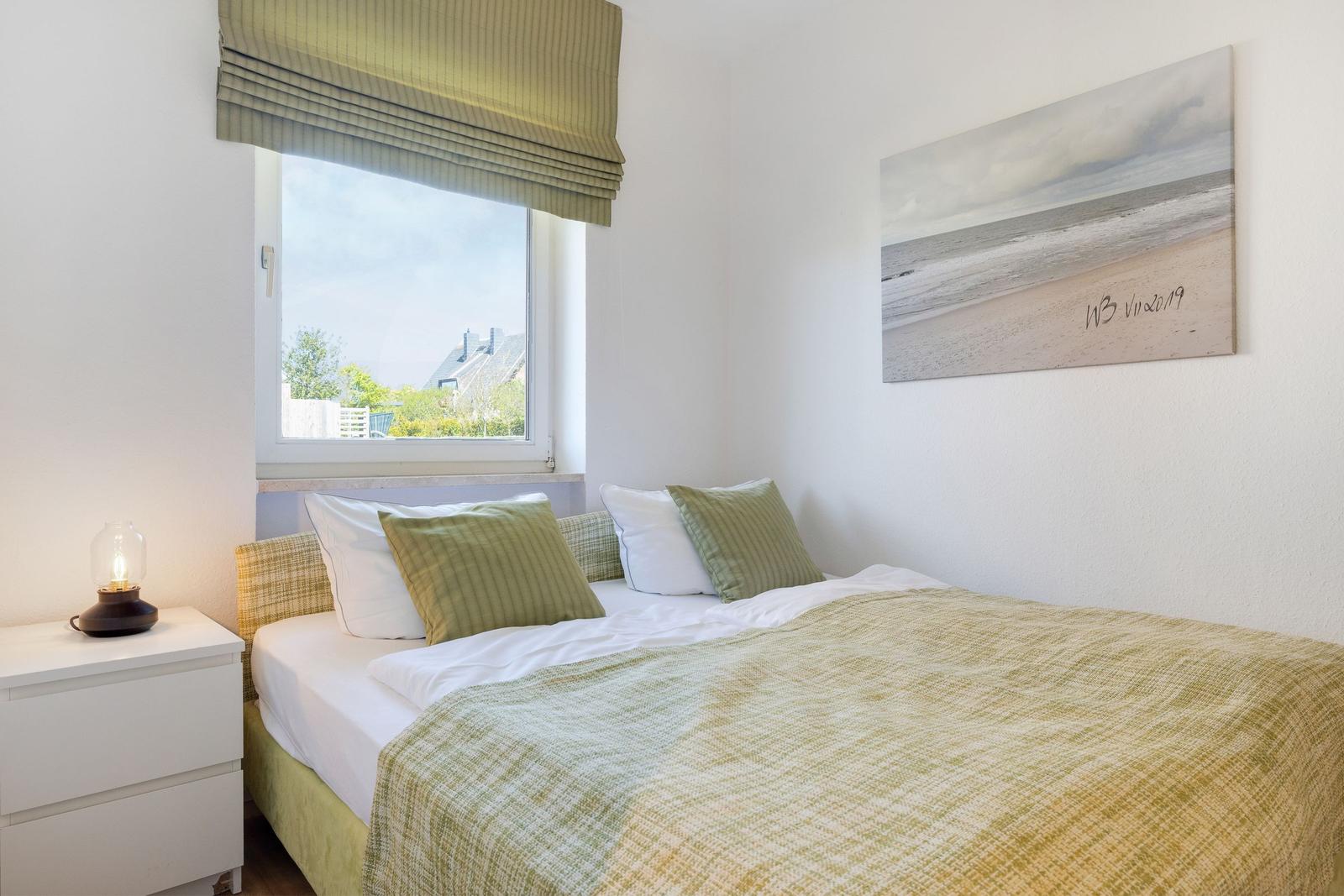 Bedroom with bed, nightstand, and window. Wall art shows beach.