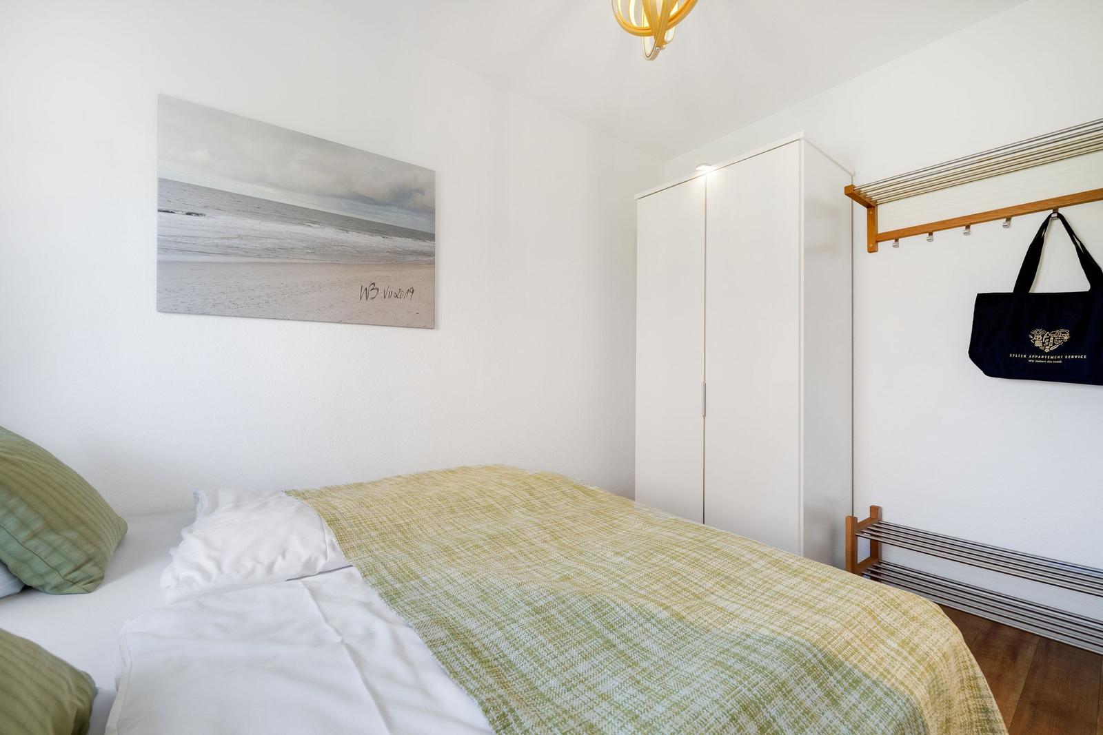 Bedroom with bed, coat rack, and wall picture on the wall.