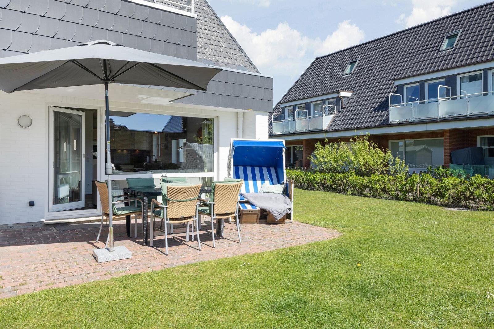 Terrace with table, chairs, and umbrella. Lawn and beach chair in background.
