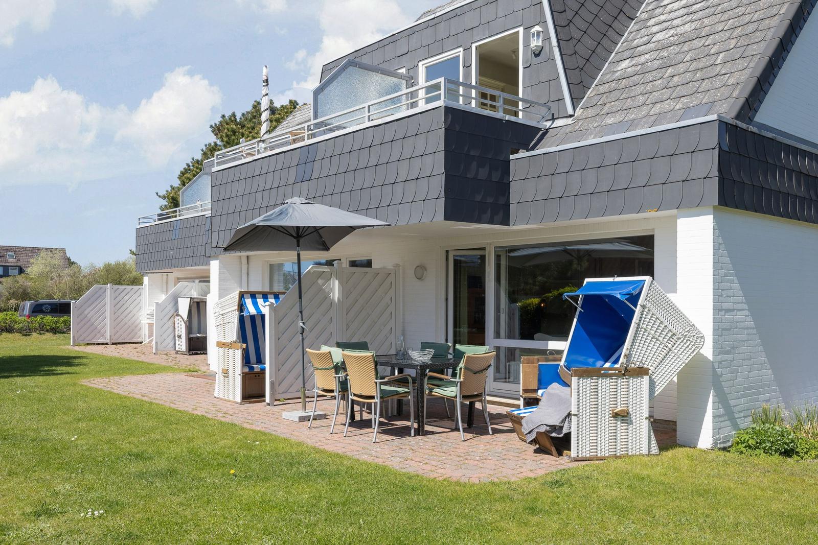 Terrace with table, chairs, and beach chairs in front of a house with balcony.