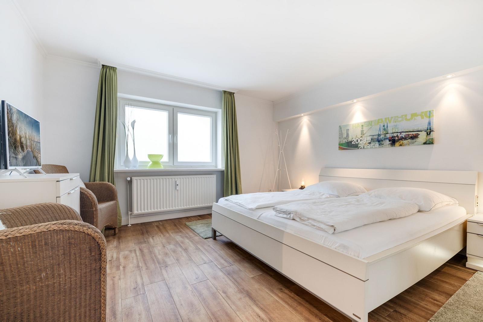 Bedroom with white bed, wooden floor, and window with green curtains.