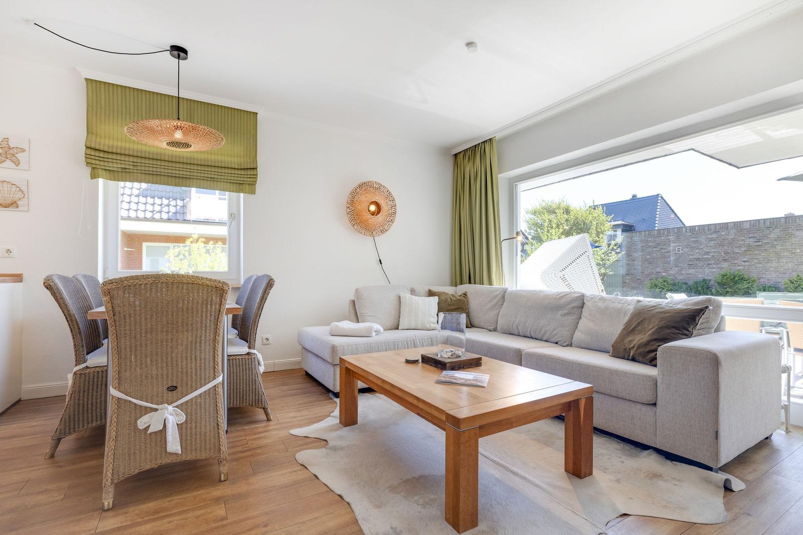 Living and dining area with sofa, table and chairs. Large windows and green curtains.