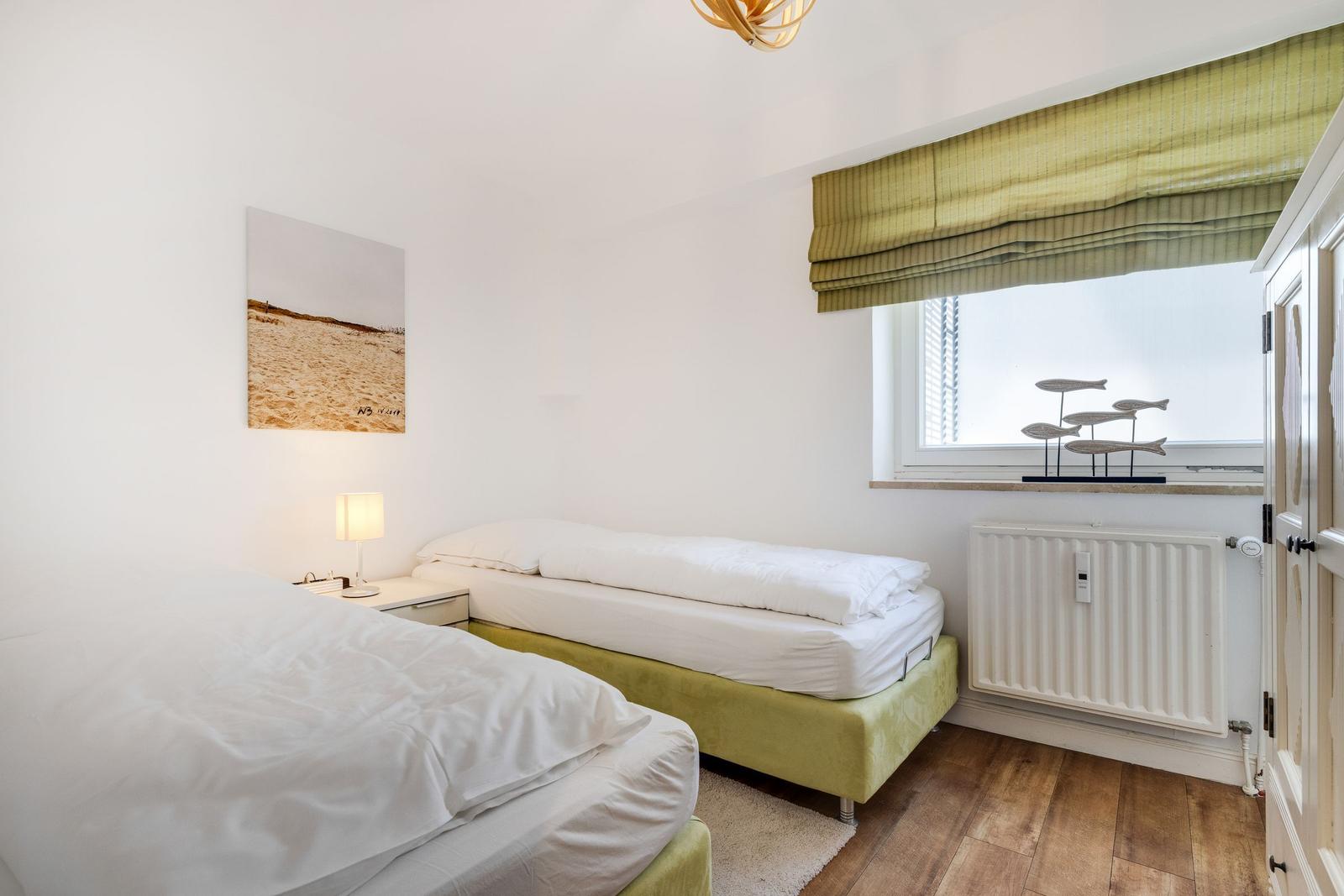 Two beds with white linens, window with green roller blind and wall art.