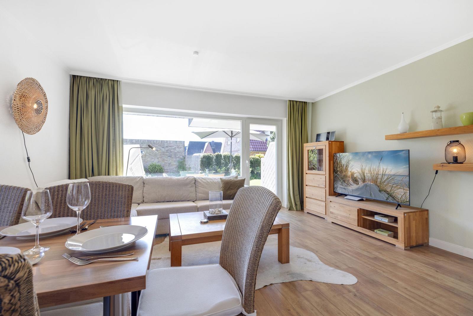 Living and dining area with wooden furniture, TV, and view of the garden.