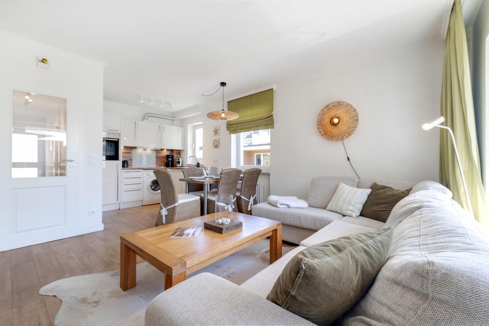 Living area with sofa, table, and kitchen area in the background.