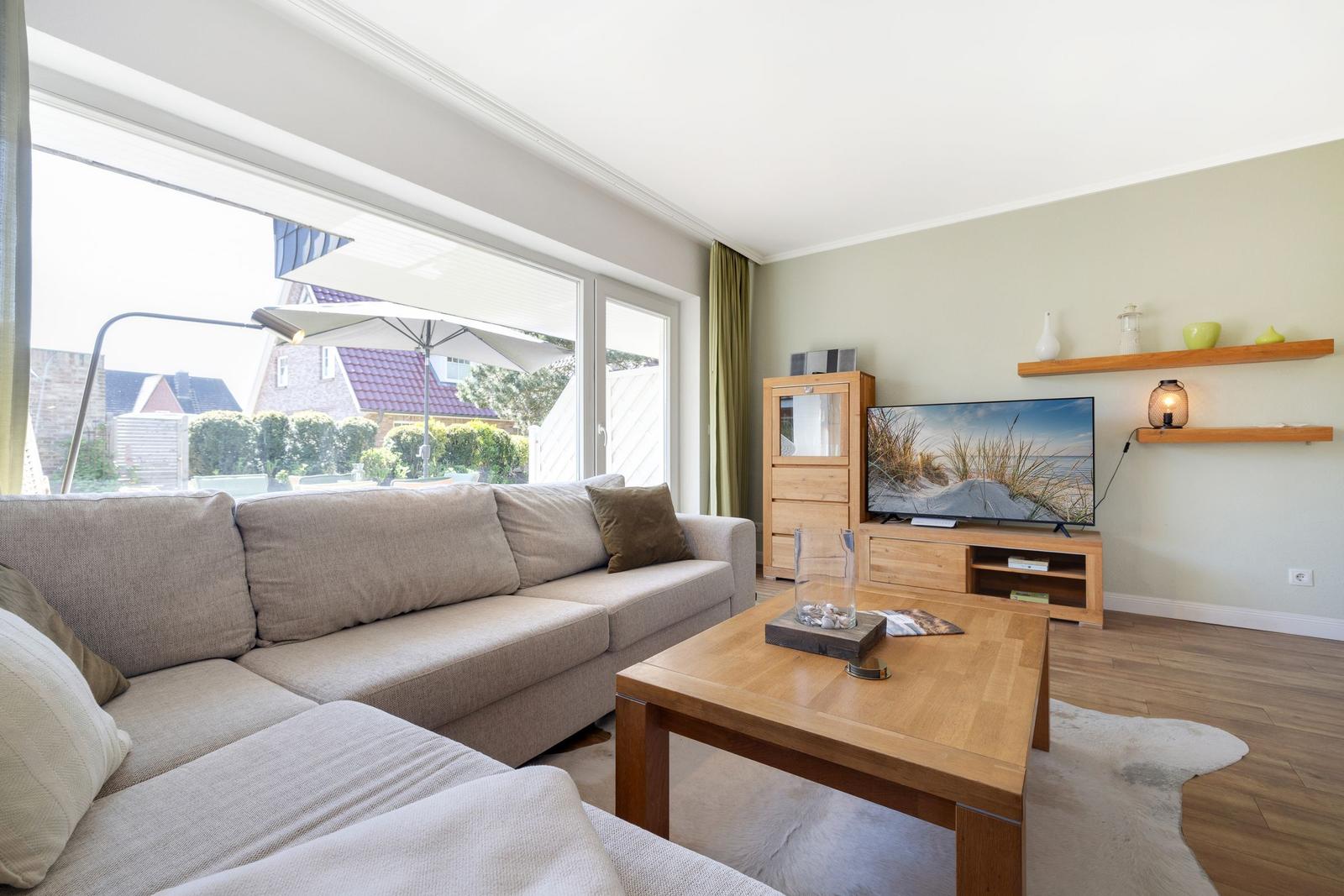 Living room with sofa, wooden table, and TV. Access to garden with umbrella.