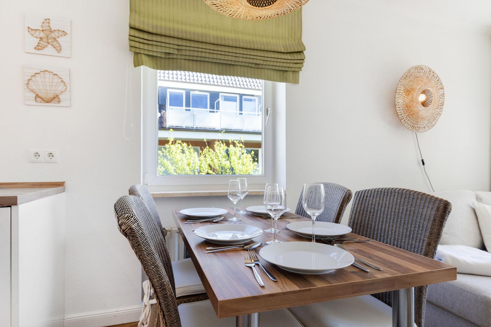 Dining room with table, chairs, and window view. Wall decor and ceiling light.