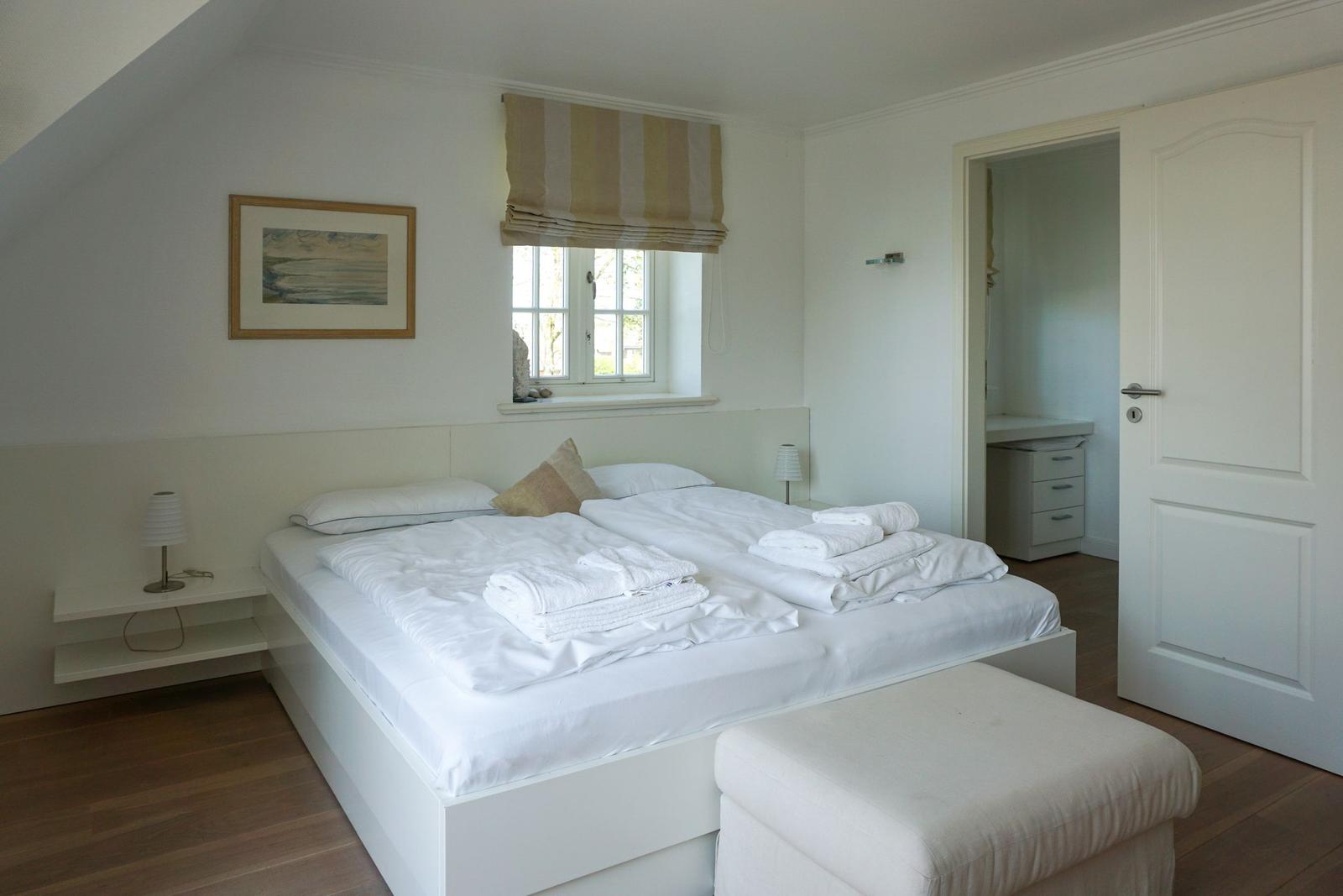 Ein Schlafzimmer mit Doppelbett, Fenster und Tür zum Ankleidezimmer.
