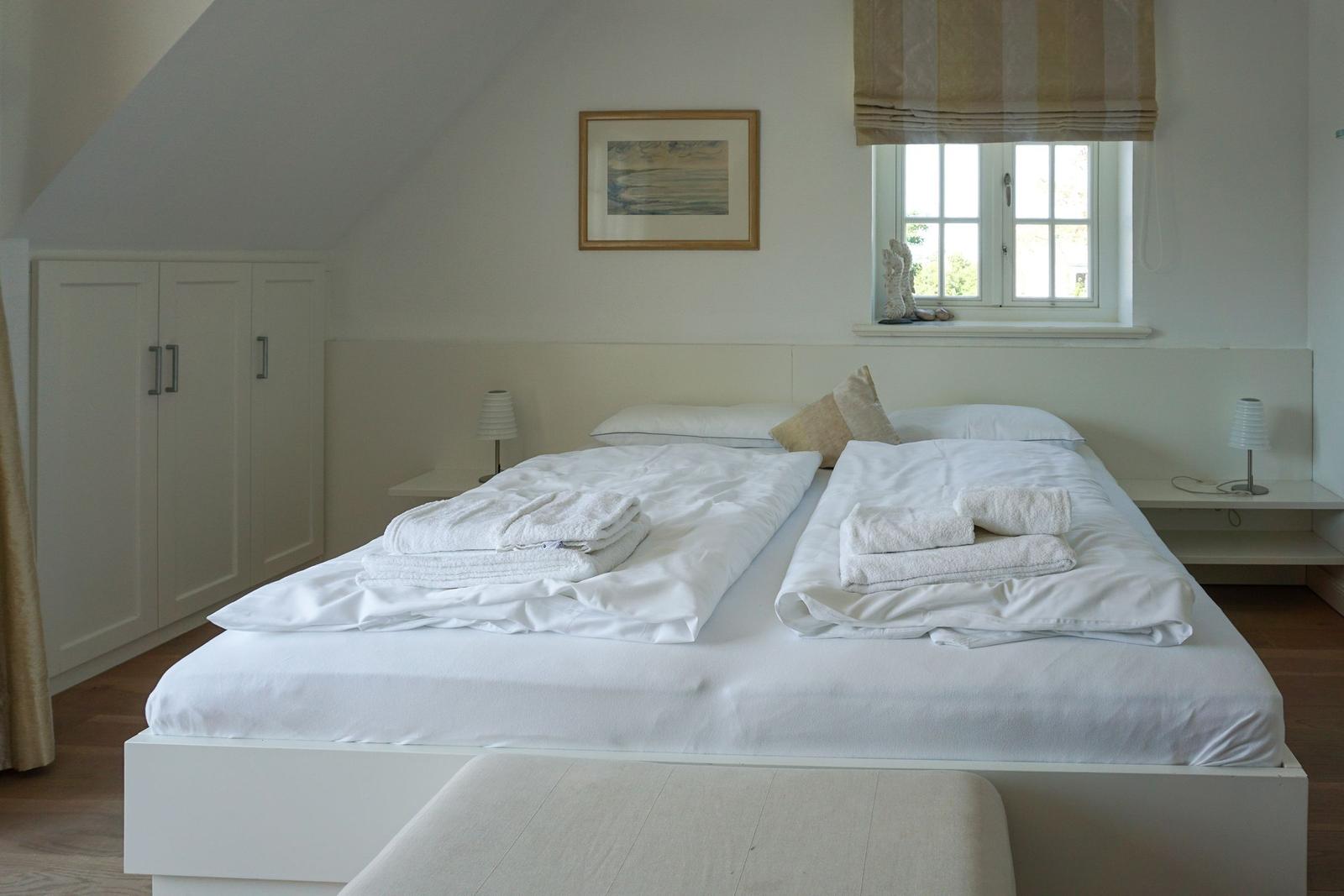 Schlafzimmer mit Doppelbett, Fenster und Kleiderschrank.