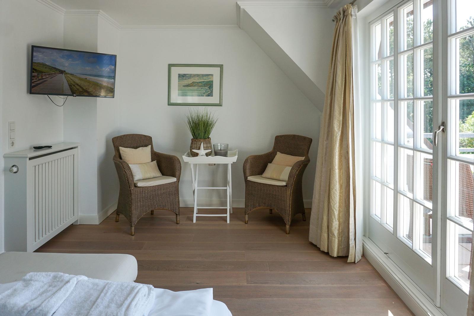 Zimmer mit zwei Stühlen, Tisch, TV und großem Fenster zur Terrasse.